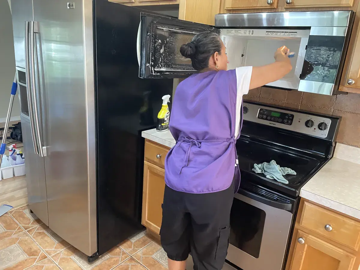 CleanieUp team member in a purple vest cleaning a microwave during a deep cleaning in Winter Garden, FL